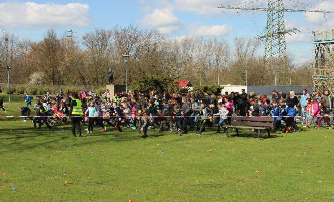 Kinder und Erwachsene starten gemeinsam einen Lauf im Freien, umgeben von buntem Gras und Bäumen.