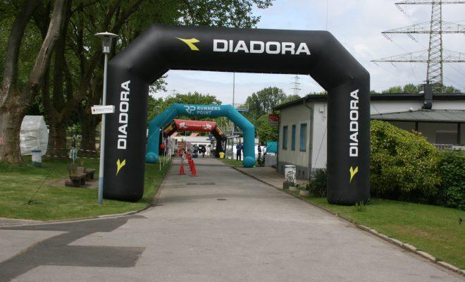 Zwei gro&szlig;e, aufblasbare Startb&ouml;gen mit den Logos &bdquo;DIADORA&ldquo; und &bdquo;RUNNERS POINT&ldquo; stehen auf einem Weg in einem Park.