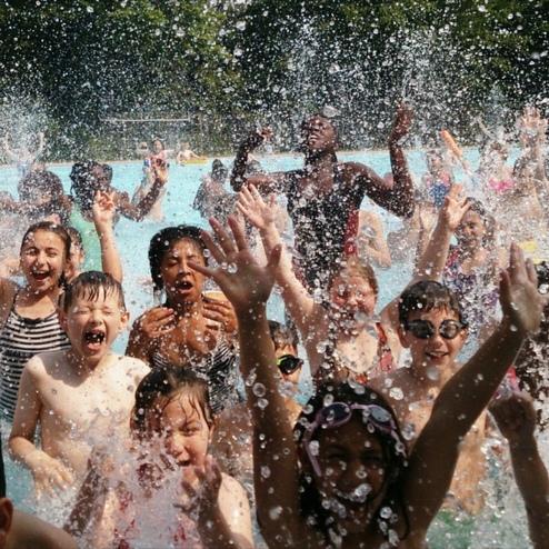 Gruppe von Kindern und Jugendlichen im Wasser, die Spa&szlig; haben und mit H&auml;nden nach oben in die Luft springen.