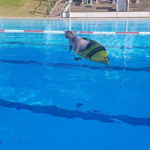 Person mit einer aufblasbaren Matte im Wasser eines Schwimmbeckens an einem sonnigen Tag.