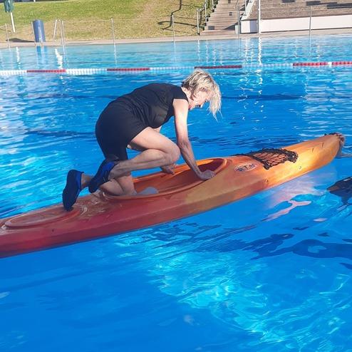 Eine Person klettert auf ein rotes Kajak in einem Schwimmbecken mit klarem blauen Wasser.