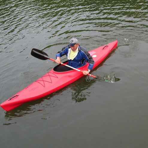 Ein Mann paddelt in einem roten Kajak auf ruhigem Wasser.