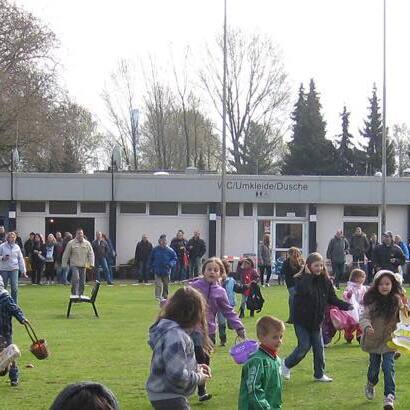 &Uuml;berf&uuml;llte Wiese mit Kindern, die spielen und an einer Umkleidekabine im Hintergrund vorbeilaufen.