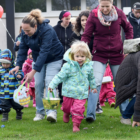 Gruppe von Kindern und Erwachsenen, die fr&ouml;hlich mit Baskets &uuml;ber eine Wiese gehen, w&auml;hrend sie an einem Event teilnehmen.