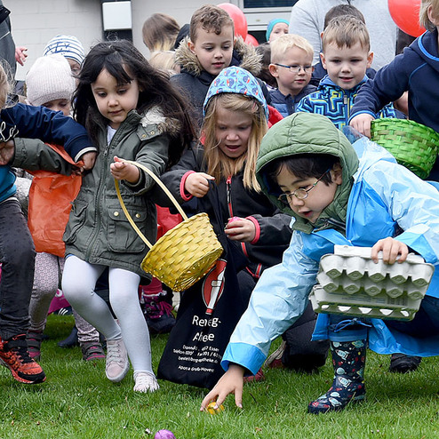 Kinder mit K&ouml;rben und Ballons suchen auf einer Wiese nach Ostereiern w&auml;hrend einer Veranstaltung im Freien.