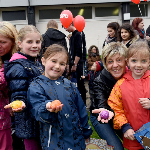 Gruppe von Kindern und Erwachsenen auf einem Festival, einige halten bunte Eier in den H&auml;nden.