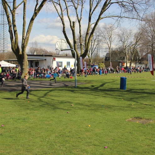 Kindern beim Rennen auf einer Wiese, umgeben von vielen Zuschauern und Veranstaltungen auf einem belebten Platz.