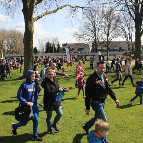 Menschenmenge auf einer Wiese, Familien und Kinder spazieren, umgeben von B&auml;umen und weiteren Besuchern.