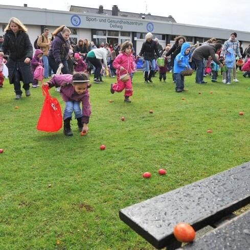 Kinder sammeln bunte Eier auf einer Wiese vor dem Sport- und Gesundheitszentrum in Delwig. Zuschauer beobachten das Geschehen.