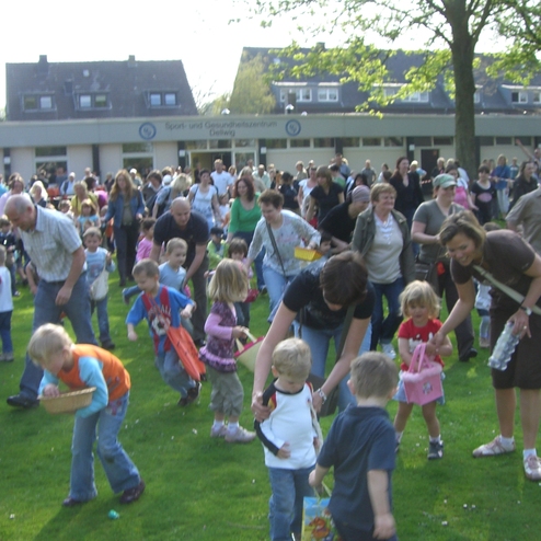 Gro&szlig;e Menschenmenge mit Kindern beim Ostereiersuchen auf einer Wiese an einem sonnigen Tag.
