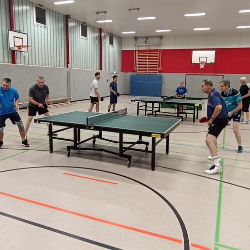 Tischtennistraining in einer Halle mit mehreren Spielern an zwei Tischtennisplatten.