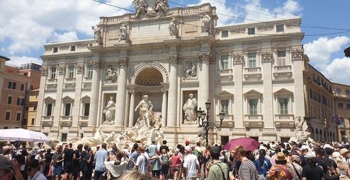 Menschenmenge vor der Fontana di Trevi, beeindruckende barocke Architektur umgeben von blauen Himmel und Wolken.