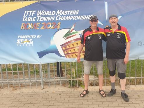 Zwei Männer in Tischtenniskleidung stehen vor einem Banner der ITTF World Masters Table Tennis Championships in Rom.
