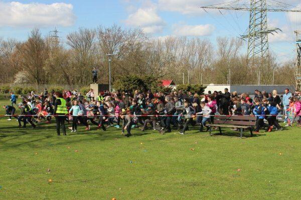 Kinder und Erwachsene starten gemeinsam einen Lauf im Freien, umgeben von buntem Gras und Bäumen.