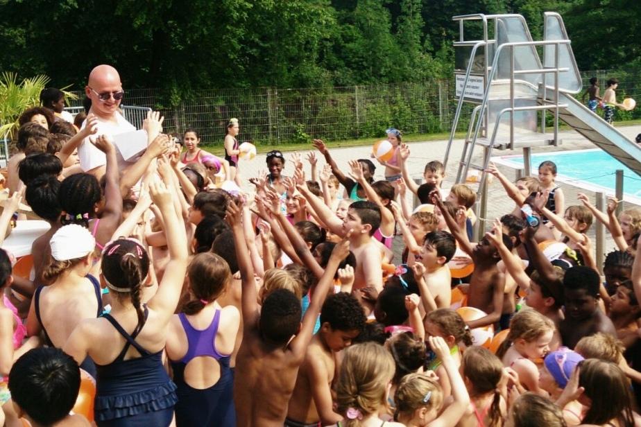 Gruppierung von Kindern mit Schwimmhilfen, die mit Freude einen Erwachsenen am Pool umringen.