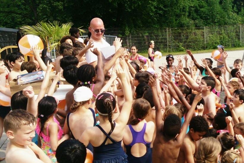 Gruppierung von Kindern mit Schwimmhilfen, die mit Freude einen Erwachsenen am Pool umringen.