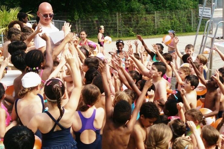 Gruppierung von Kindern mit Schwimmhilfen, die mit Freude einen Erwachsenen am Pool umringen.