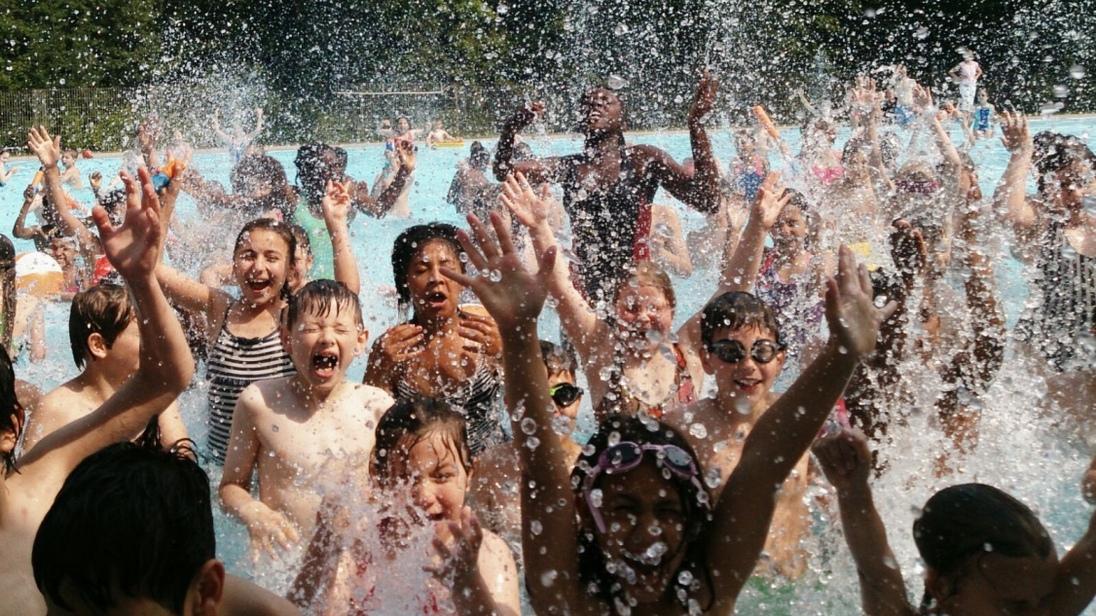 Gruppe von Kinder im Wasser, spritzend und lachend, mit erhobenen H&auml;nden in einem Schwimmbad.