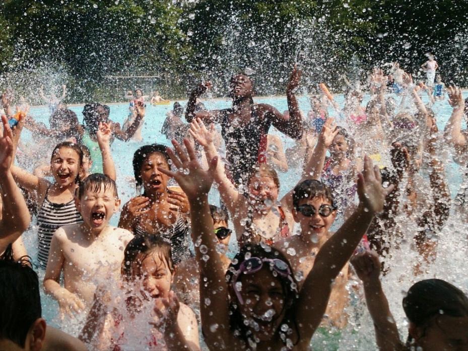Gruppe von Kinder im Wasser, spritzend und lachend, mit erhobenen H&auml;nden in einem Schwimmbad.