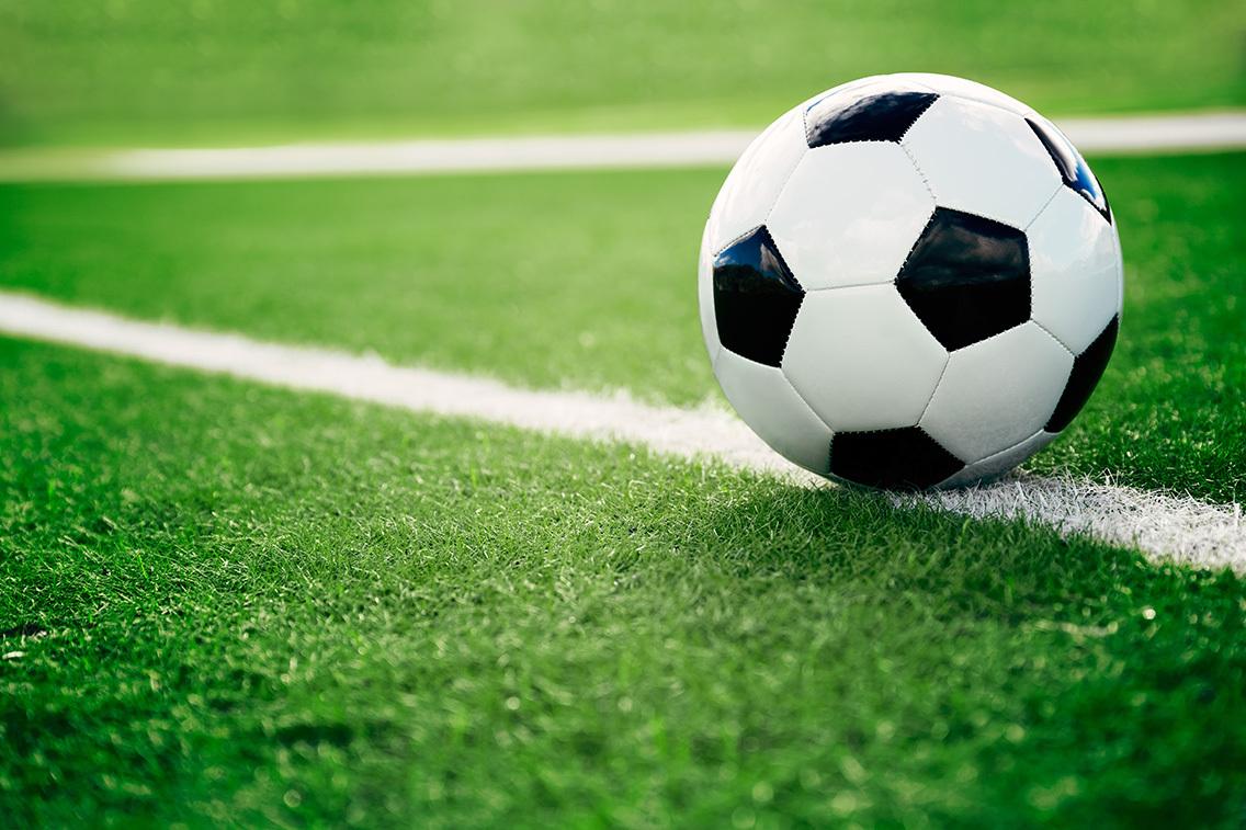 Nahaufnahme eines Fu&szlig;balles auf gr&uuml;nem Kunstrasen neben einer wei&szlig;en Spielfeldlinie.