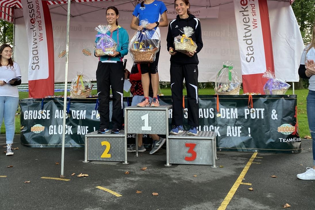 Drei Sportlerinnen stehen auf dem Siegertreppchen, w&auml;hrend sie Medaillen und Preise pr&auml;sentieren.