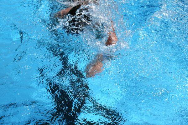 Schwimmer taucht ins Wasser, Arm zieht durch die hellblaue Wasseroberfl&auml;che, Spritzwasser bildet Wellen.