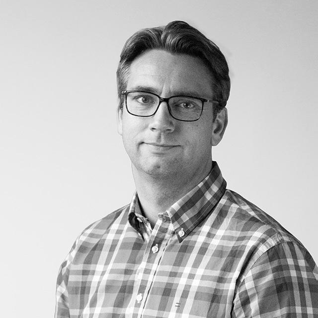 Porträt eines Mannes mit Brille, der ein kariertes Hemd trägt, vor einem neutralen Hintergrund.