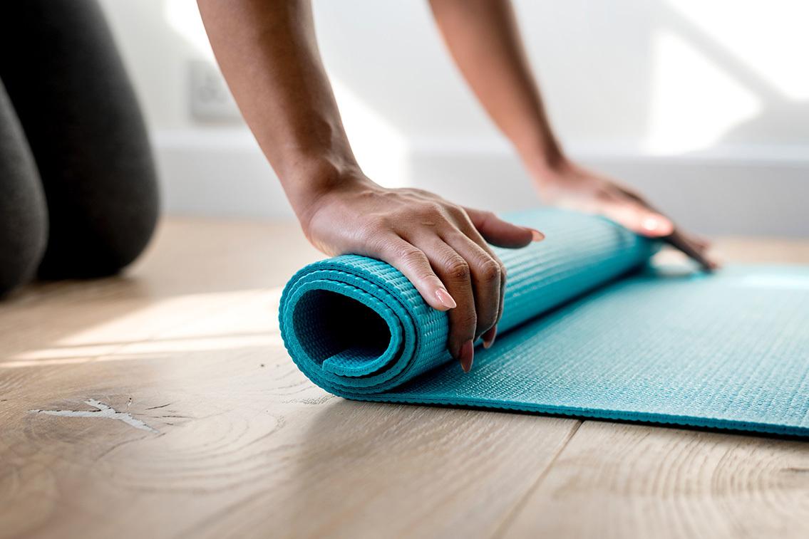 Eine Person rollt eine turquoise Yogamatte auf einem Holzfußboden zusammen.