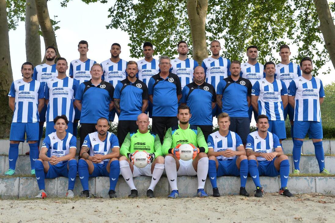 Mannschaftsfoto einer Fu&szlig;ballmannschaft in blauen und wei&szlig;en Trikots, auf einer Treppe im Freien posierend.