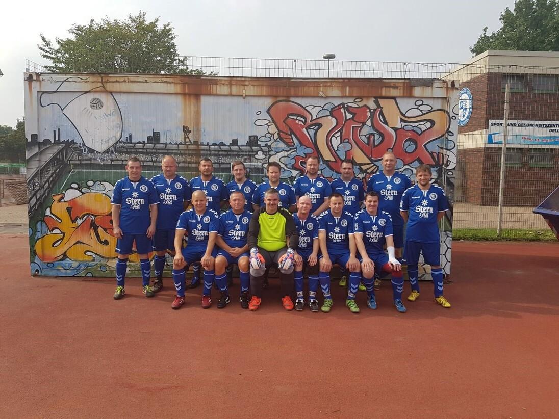Grupp portrait eines Fußballteams in blauen Trikots vor einer graffiti-bemalten Wand auf einem Sportplatz.