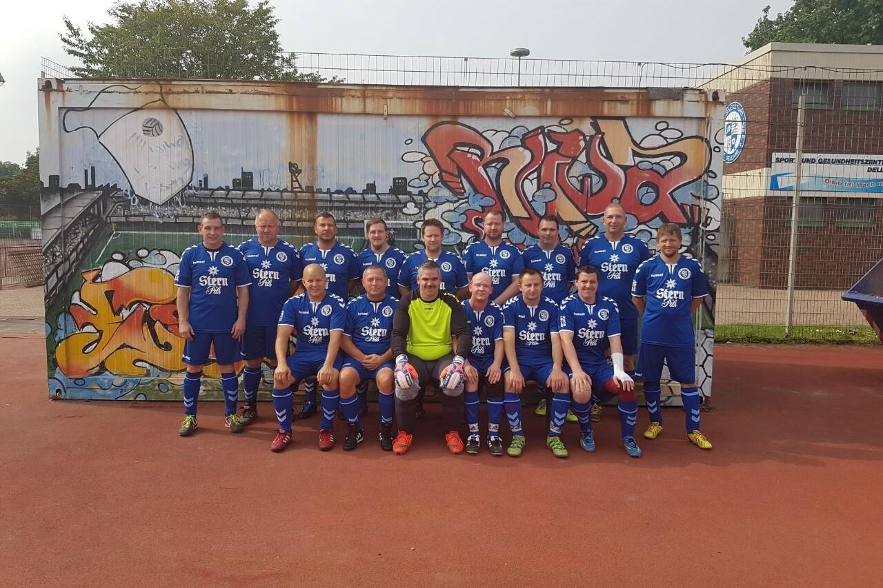 Grupp portrait eines Fu&szlig;ballteams in blauen Trikots vor einer graffiti-bemalten Wand auf einem Sportplatz.