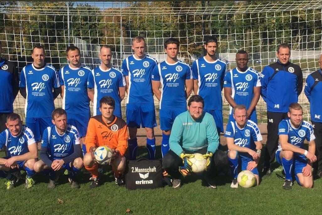 Mannschaftsfoto einer Fu&szlig;ballmannschaft in blauen Trikots vor einem Tor auf einem gr&uuml;nen Platz.
