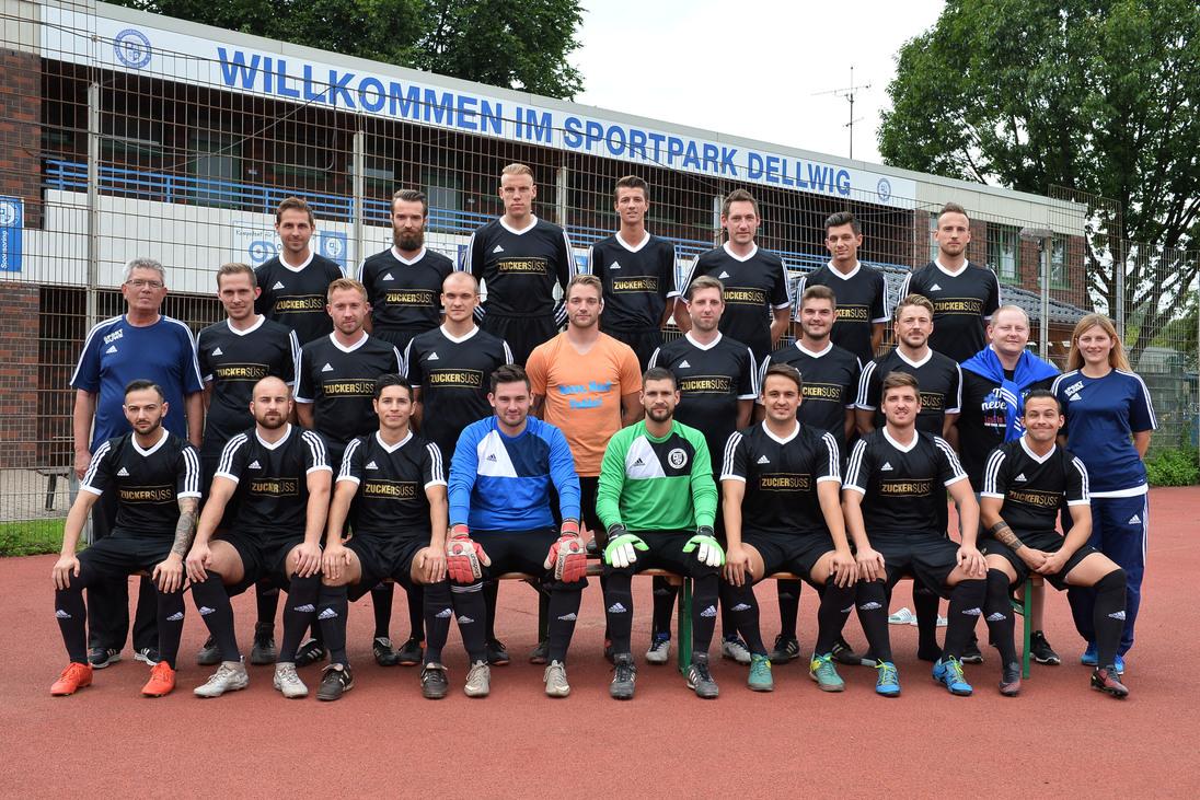 Mannschaftsfoto einer Fu&szlig;ballmannschaft in schwarzen Trikots, stehend und sitzend, vor einem Sportpark.