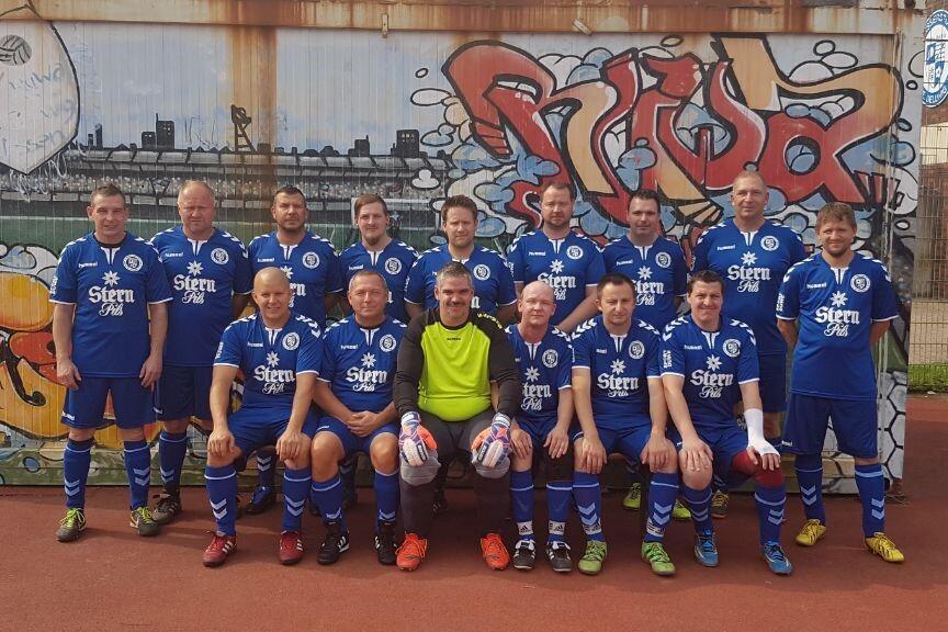 Grupp portrait eines Fußballteams in blauen Trikots vor einer graffiti-bemalten Wand auf einem Sportplatz.