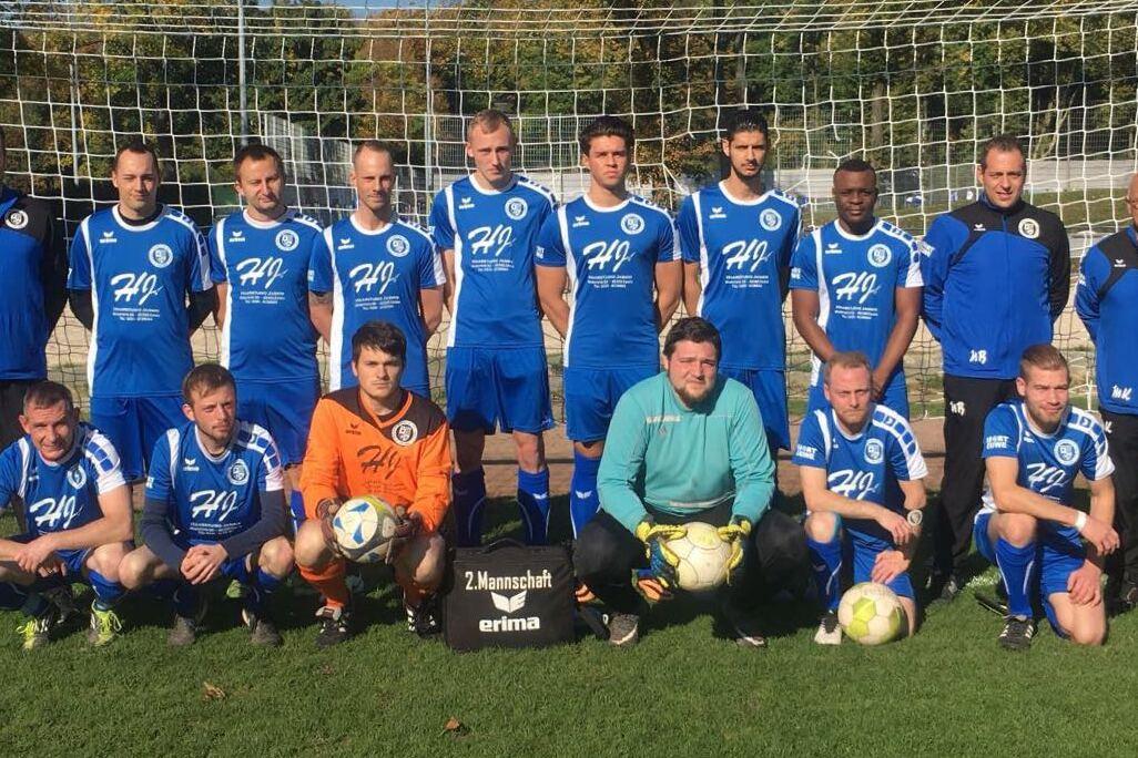 Mannschaftsfoto einer Fußballmannschaft in blauen Trikots vor einem Tor auf einem grünen Platz.