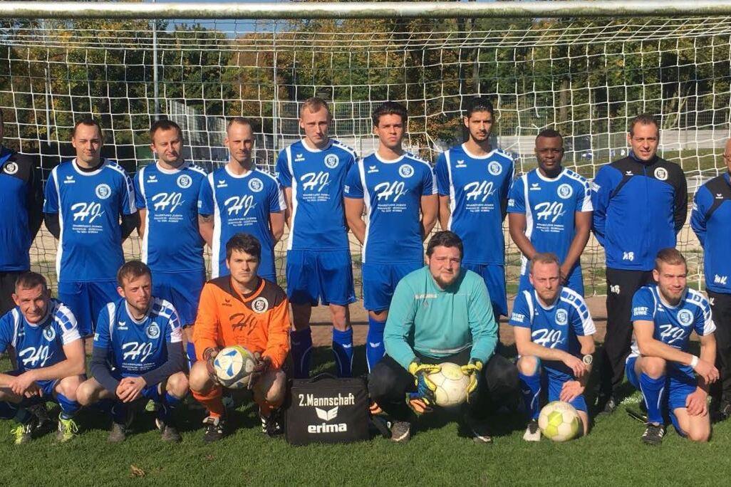 Mannschaftsfoto einer Fu&szlig;ballmannschaft in blauen Trikots vor einem Tor auf einem gr&uuml;nen Platz.