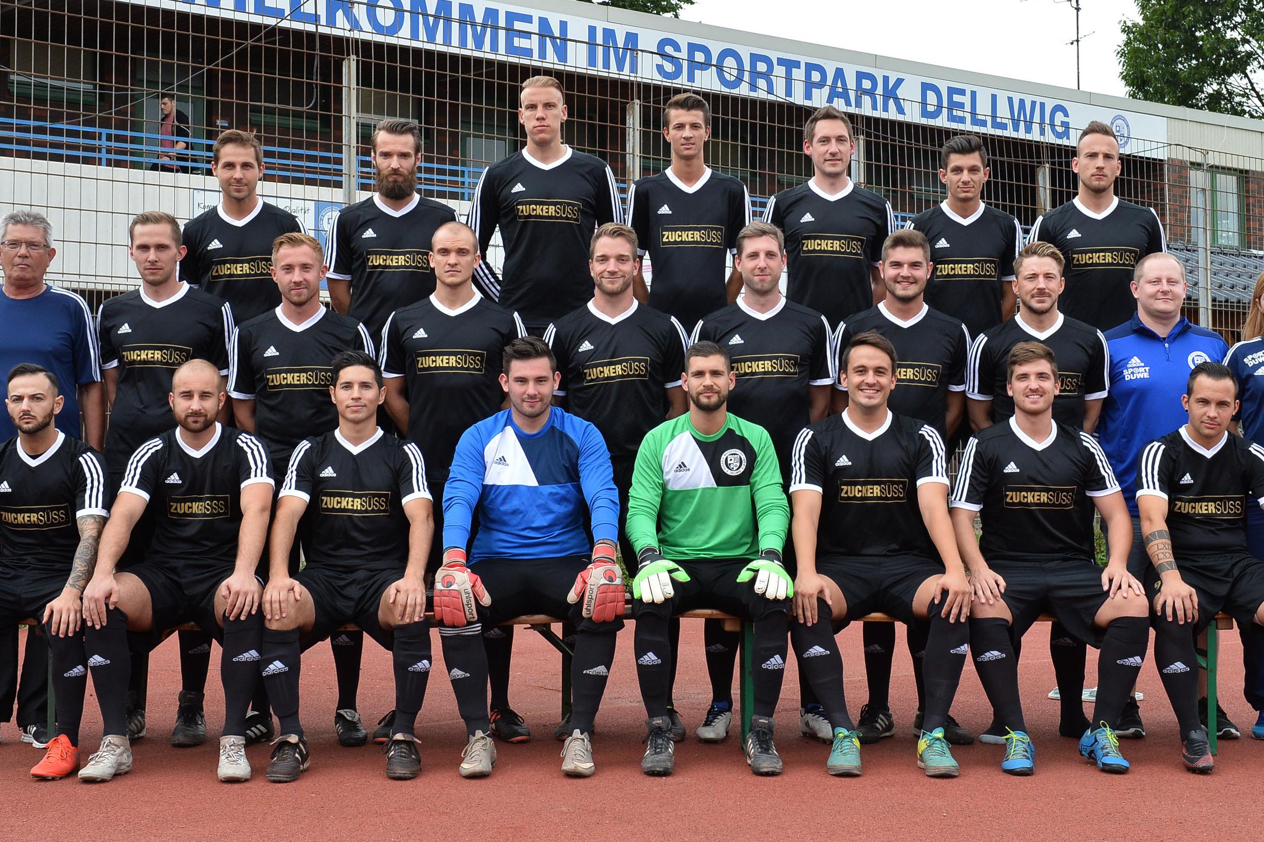 Gruppenfoto einer Fu&szlig;ballmannschaft in schwarz-wei&szlig;er Sportkleidung im Sportpark Dellwig vor einem Begr&uuml;&szlig;ungsschild.