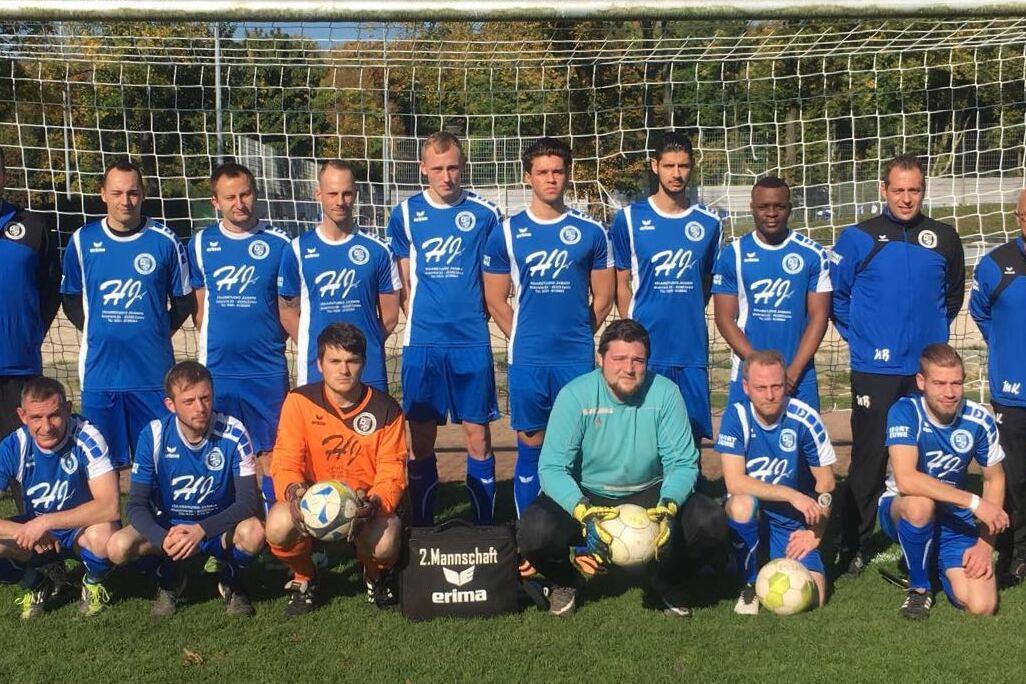 Mannschaftsfoto einer Fußballmannschaft in blauen Trikots vor einem Tor auf einem grünen Platz.