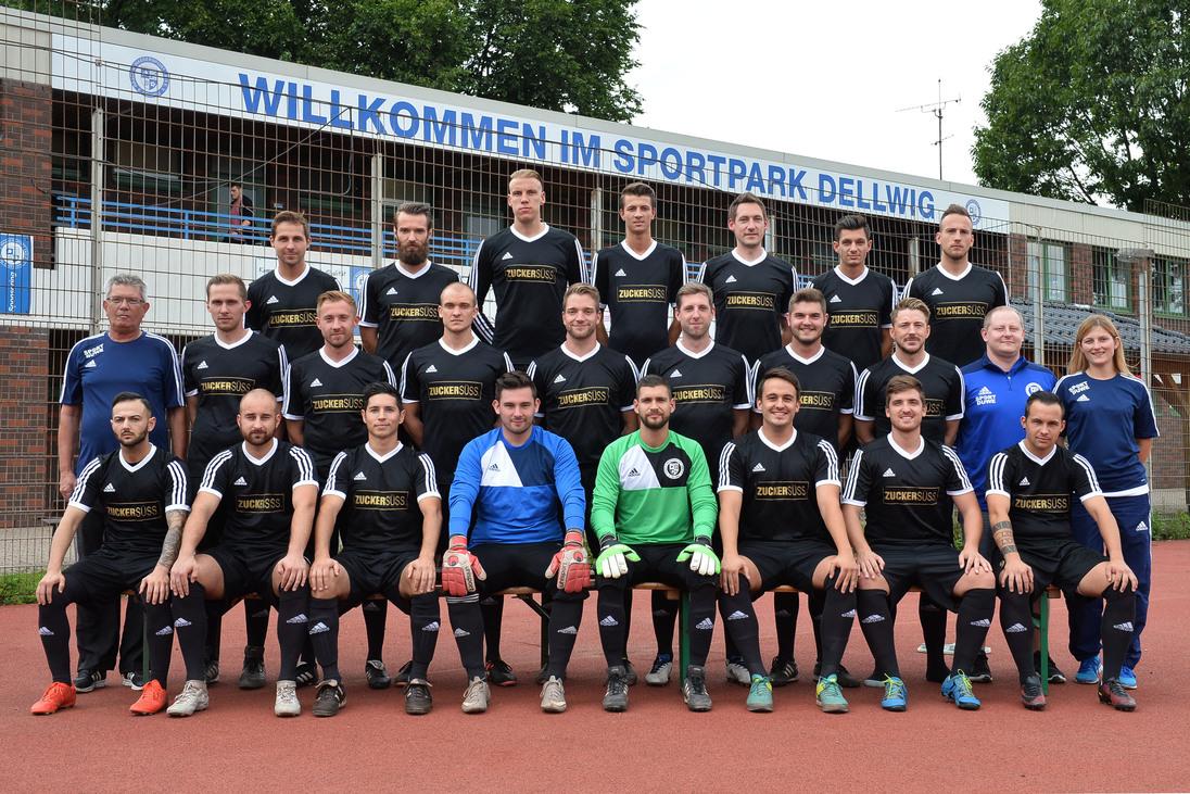 Gruppenfoto einer Fu&szlig;ballmannschaft in schwarz-wei&szlig;er Sportkleidung im Sportpark Dellwig vor einem Begr&uuml;&szlig;ungsschild.