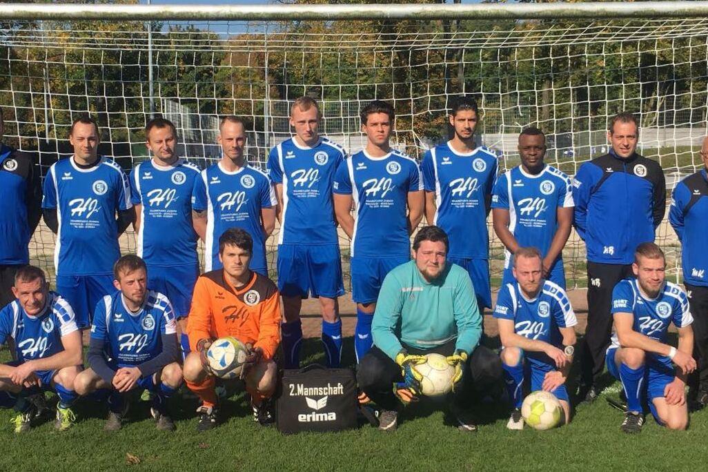 Mannschaftsfoto einer Fu&szlig;ballmannschaft in blauen Trikots vor einem Tor auf einem gr&uuml;nen Platz.