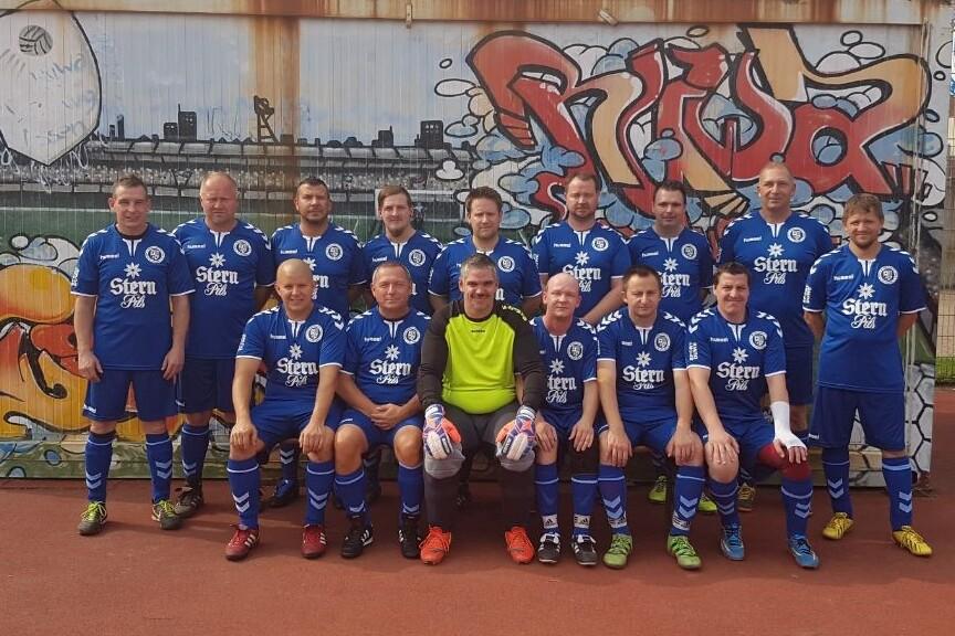 Grupp portrait eines Fußballteams in blauen Trikots vor einer graffiti-bemalten Wand auf einem Sportplatz.
