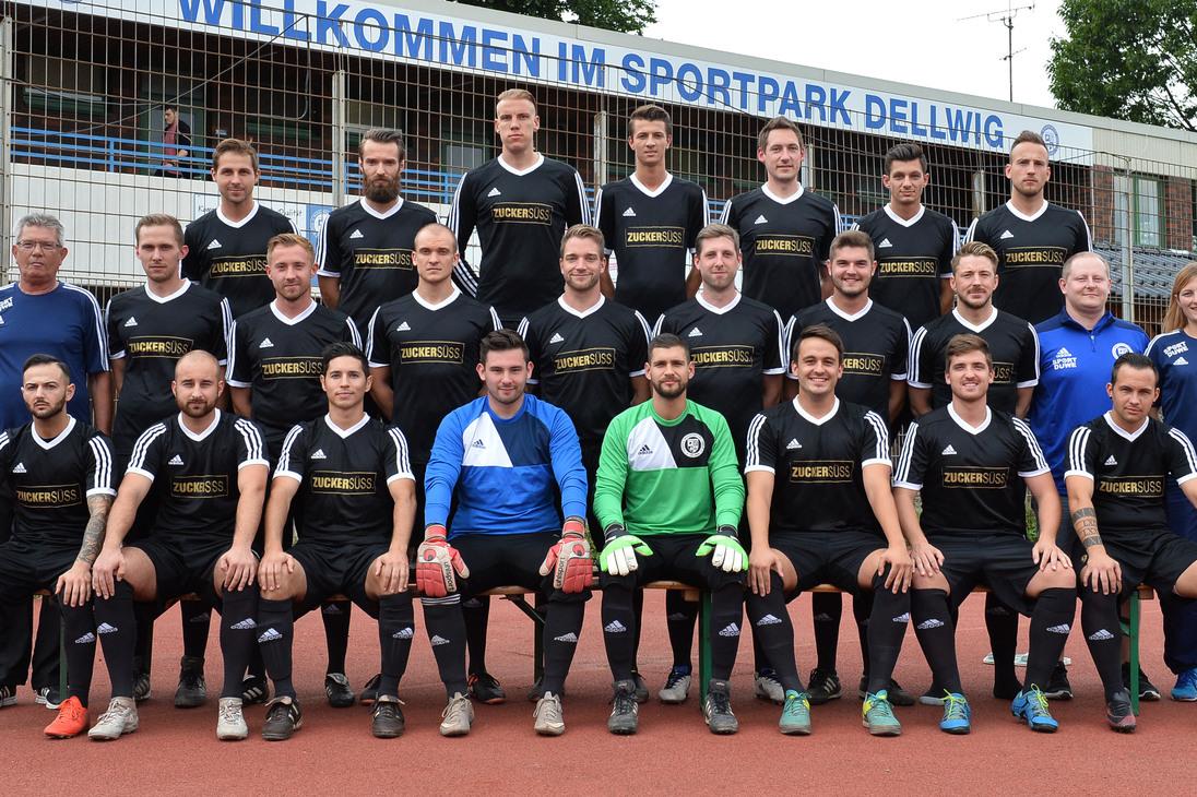 Gruppenfoto einer Fu&szlig;ballmannschaft in schwarz-wei&szlig;er Sportkleidung im Sportpark Dellwig vor einem Begr&uuml;&szlig;ungsschild.