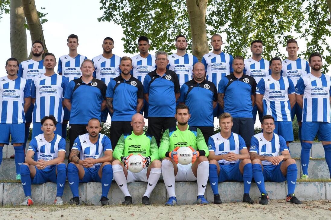 Mannschaftsfoto einer Fu&szlig;ballmannschaft in blauen und wei&szlig;en Trikots, auf einer Treppe im Freien posierend.