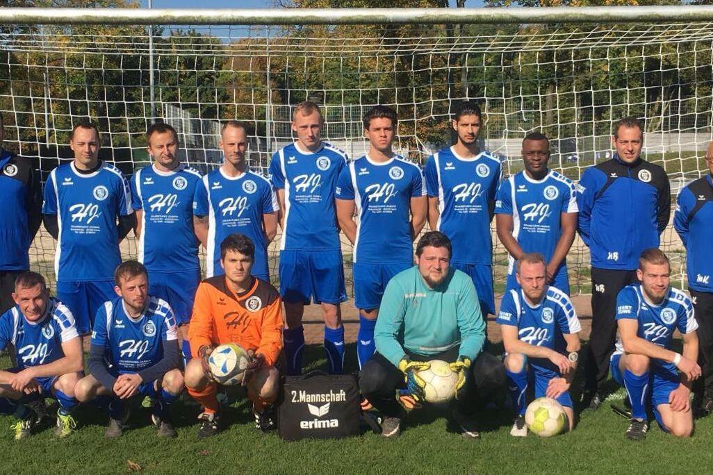 Mannschaftsfoto einer Fu&szlig;ballmannschaft in blauen Trikots vor einem Tor auf einem gr&uuml;nen Platz.
