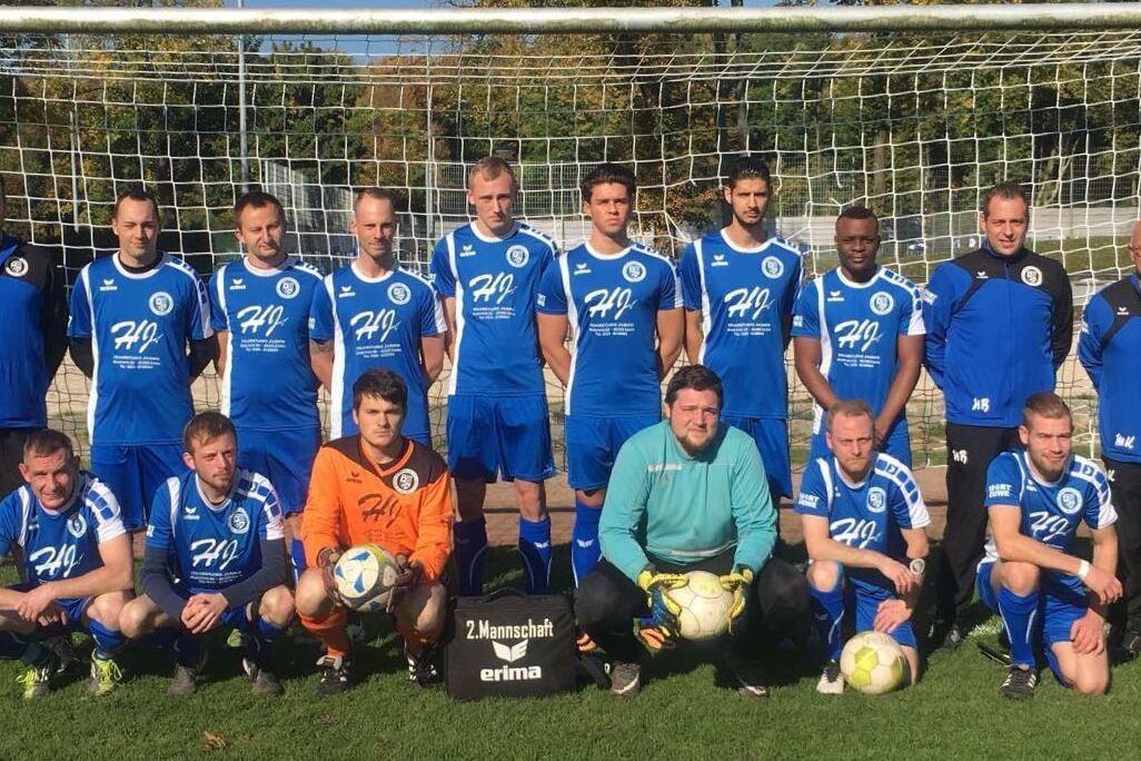 Mannschaftsfoto einer Fußballmannschaft in blauen Trikots vor einem Tor auf einem grünen Platz.
