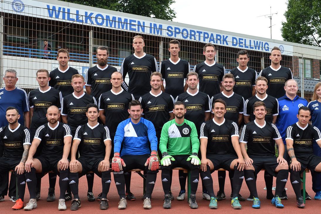Gruppenfoto einer Fu&szlig;ballmannschaft in schwarz-wei&szlig;er Sportkleidung im Sportpark Dellwig vor einem Begr&uuml;&szlig;ungsschild.