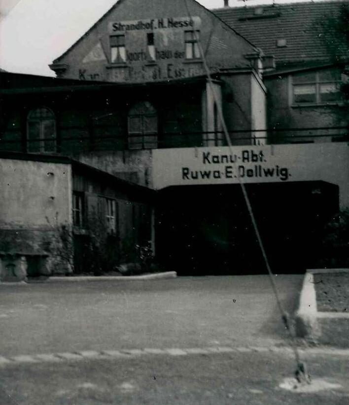 Historisches Geb&auml;ude mit der Aufschrift &bdquo;Kanu-Abt. Ruwa E. Dellwig&ldquo; auf der Fassade, umgeben von einer gepflasterten Fl&auml;che.