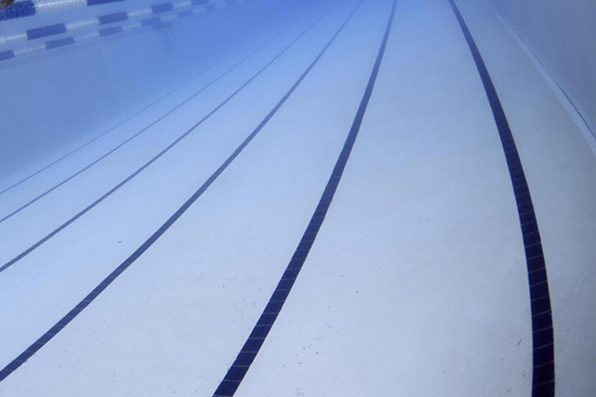 Schwimmer unter Wasser, der an einer blauen Bahn in einem Schwimmbecken vorbeizieht, mit Wellenbildung um ihn herum.