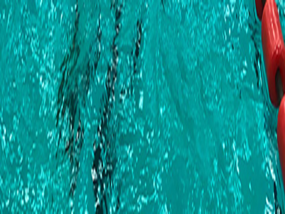 Gruppe von Schwimmern im Schwimmbecken w&auml;hrend des Trainings, mit roten Bahnmarkierungen und hellen Deckenlichtern.