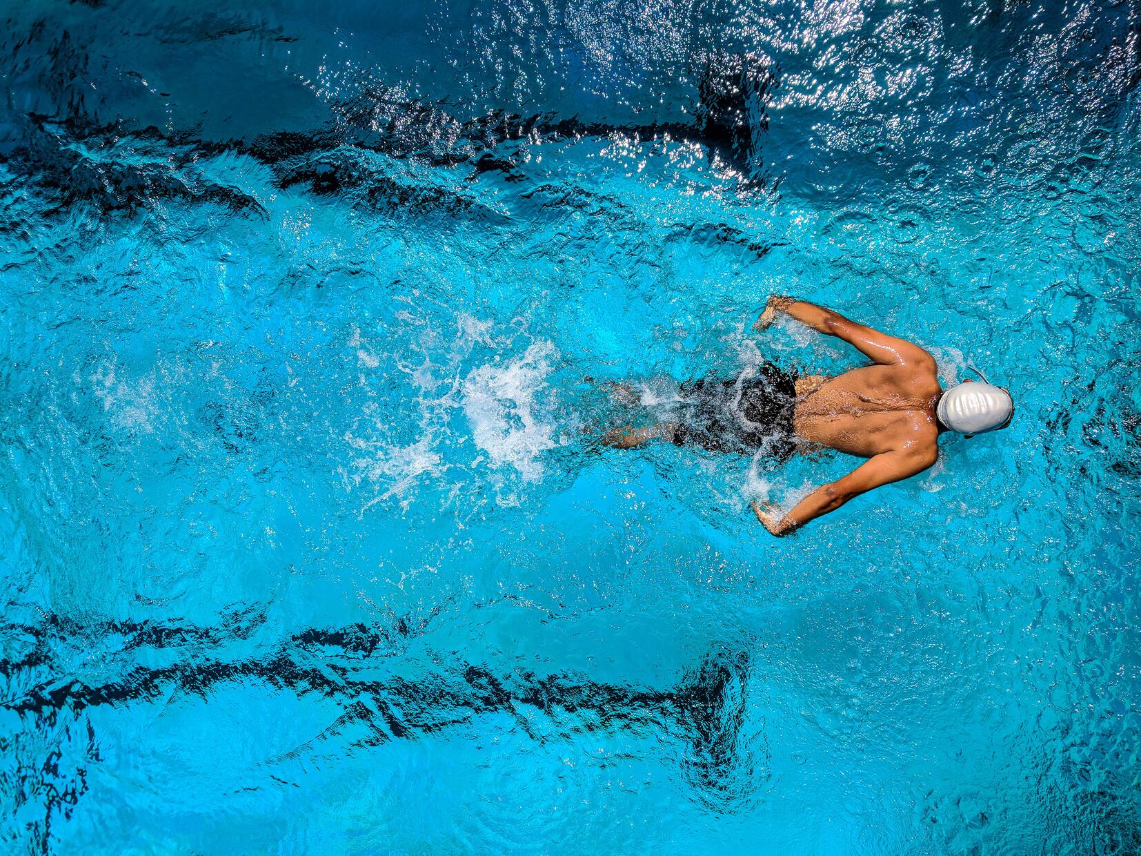Ein Schwimmer in einem wei&szlig;en Badekappen schwimmt unter Wasser in einem blauen Schwimmbecken.